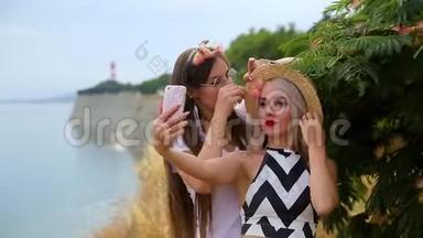 两个积极的女孩，一个戴着帽子的金发女孩，一个戴着眼镜的黑发女孩，四处闲逛，用手机拍自拍